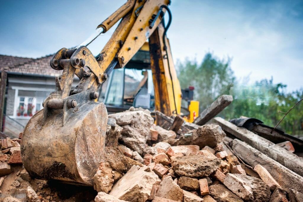 Demolition Services Quebec and Montreal with an excavator performing building teardown on a construction site, surrounded by piles of bricks, concrete debris, and partial house remains.