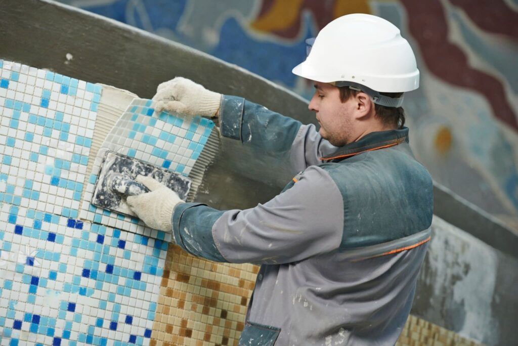 Swimming Pool Installation Quebec — worker installing blue mosaic tiles designed for swimming pools, providing a water-resistant and decorative surface made from durable materials like ceramic or glass.