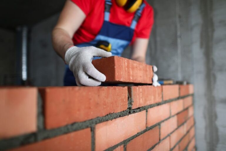 Mason laying bricks with a trowel, illustrating exterior finishings services in Quebec that focus on skilled brickwork and durable wall construction for residential and commercial buildings.