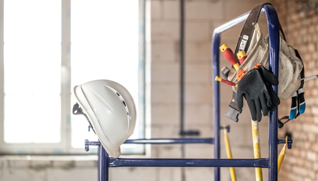Home maintenance services Quebec showing construction tools and safety gear including a white hard hat, work gloves, a tool belt with screwdrivers and hammer, and a ladder on an active job site.