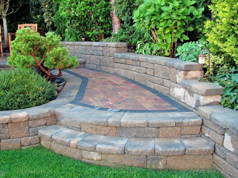 A landscaped outdoor area in Montreal featuring stone retaining wall construction as part of a hardscape design with concrete and brick elements, representing retaining wall construction Montreal.
