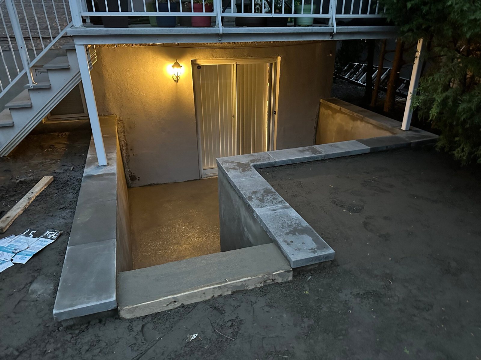Basement Walkout Services in Quebec with a view of a concrete stairway leading to a lower-level entrance featuring a glass sliding door and unfinished ground, indicating ongoing construction work.